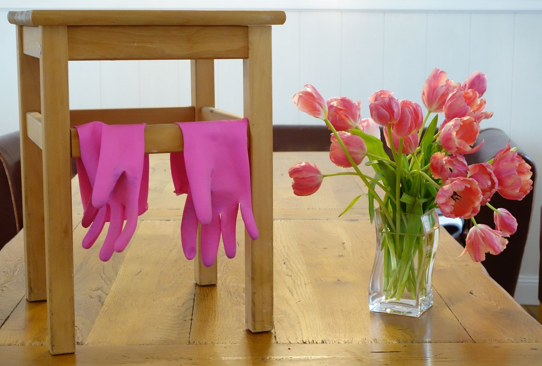 Pinke Putzhandschuhe hängen über einem Hocker neben einem Tulpenstrauß