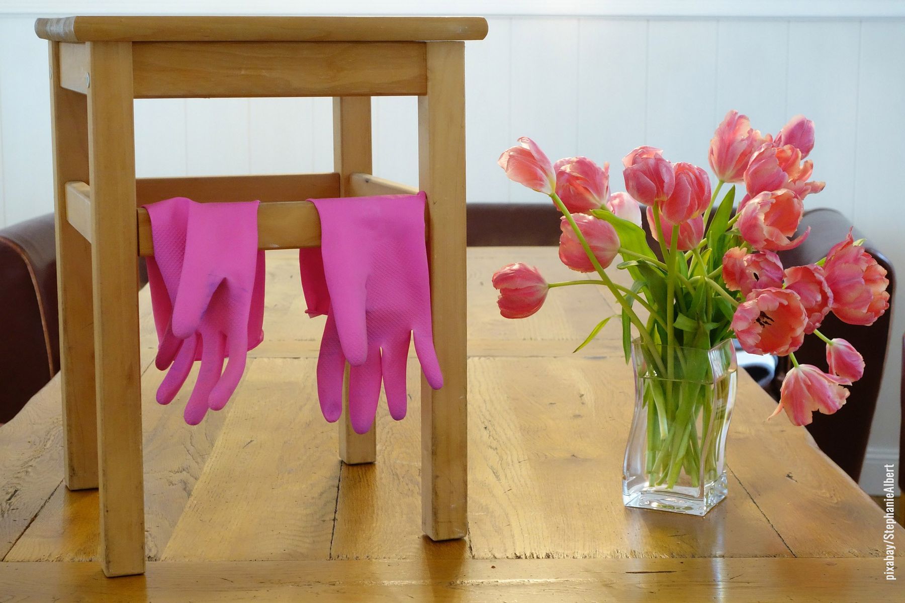 Pinke Putzhandschuhe auf Holzhocker neben rosa Tulpenstrauss