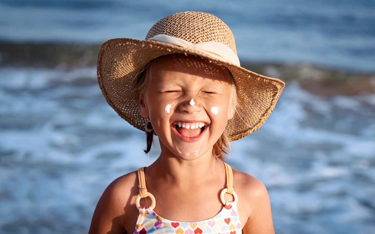 Lachendes Mädchen mit Sonnencreme im Gesicht am Strand