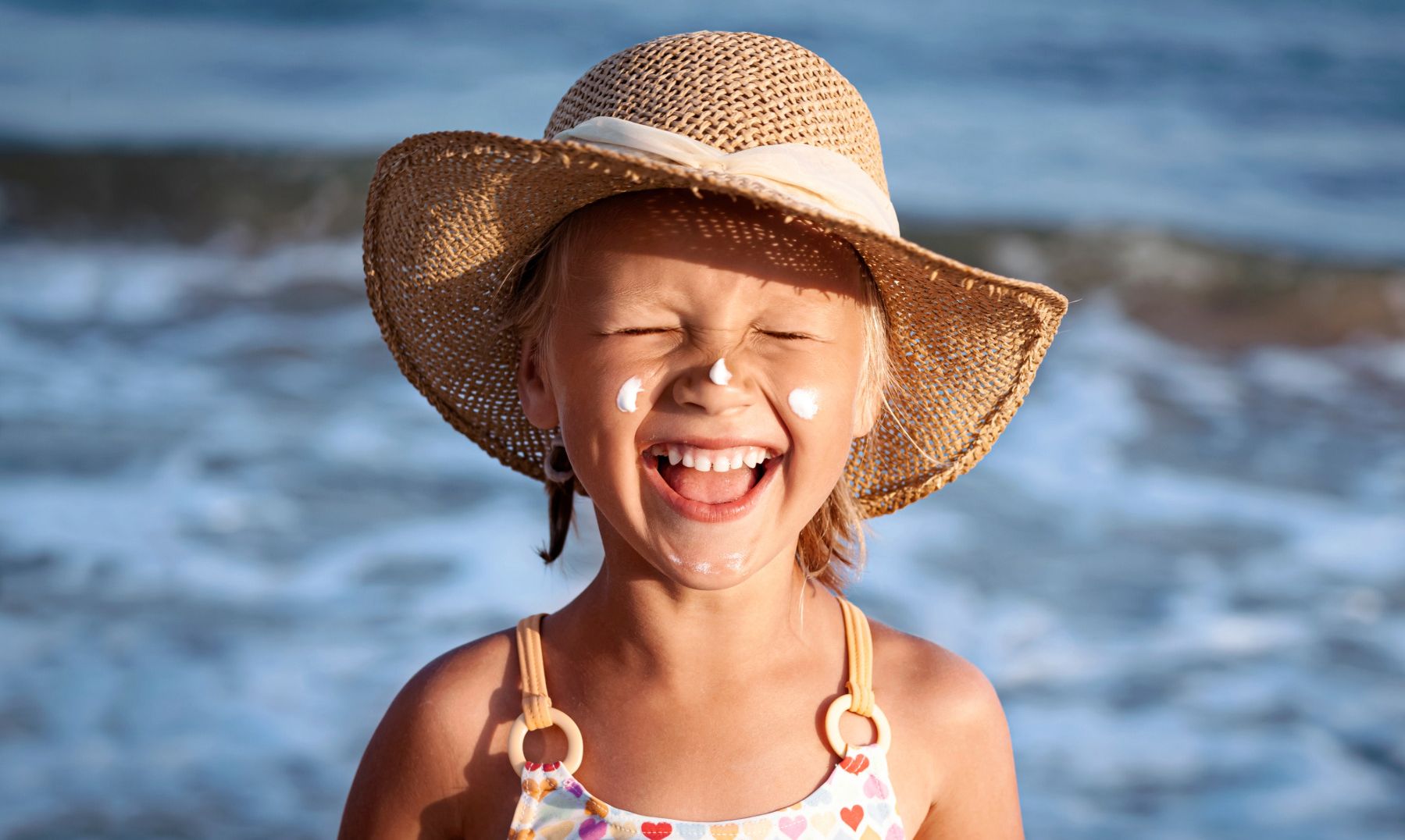 Lachendes Mädchen mit Sonnencreme im Gesicht am Strand